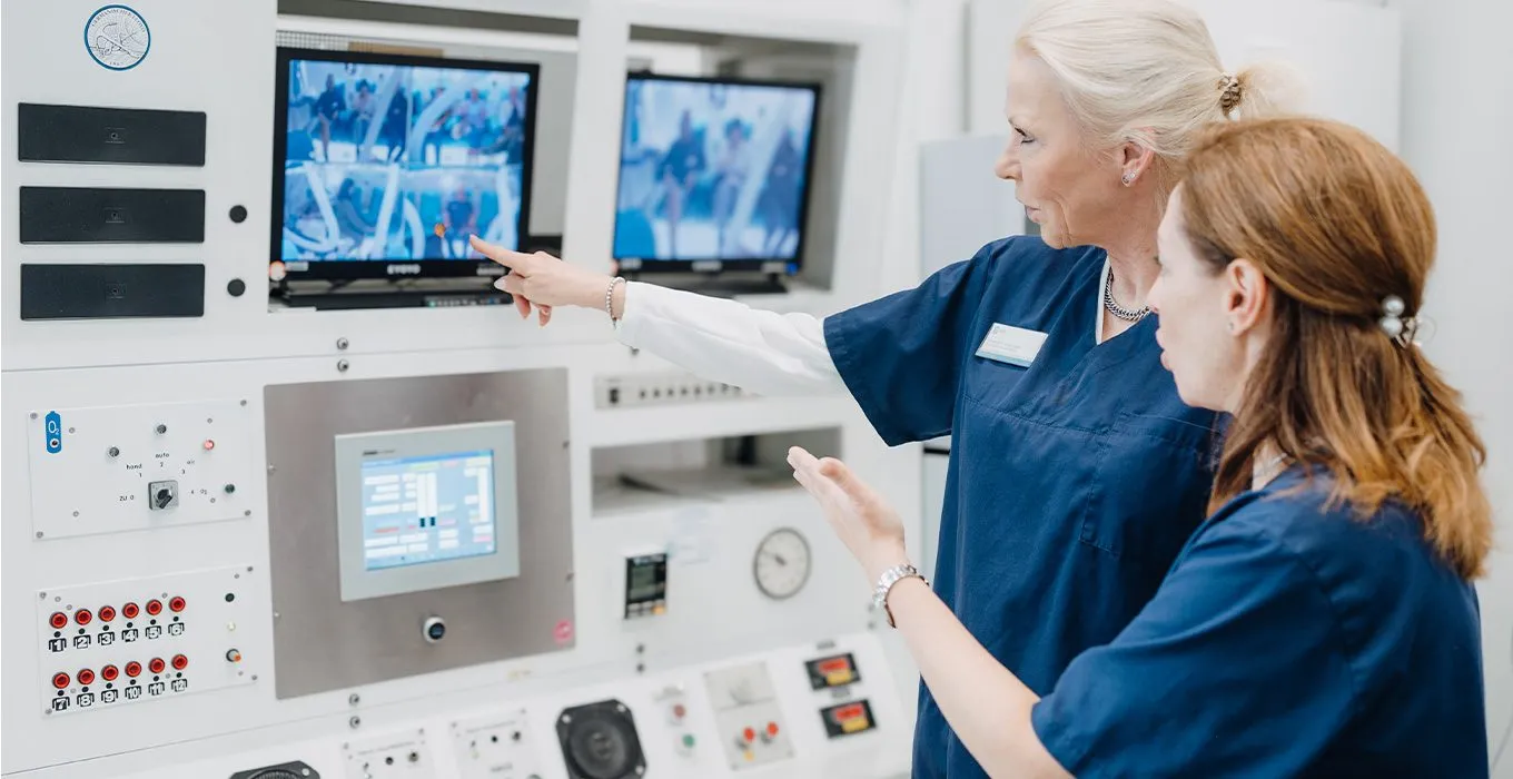 Zwei Mitarbeiterinnen am Leitstand der Druckkammer mit Monitoren und Bedienpult, HBO-Zentrum Euregio Aachen